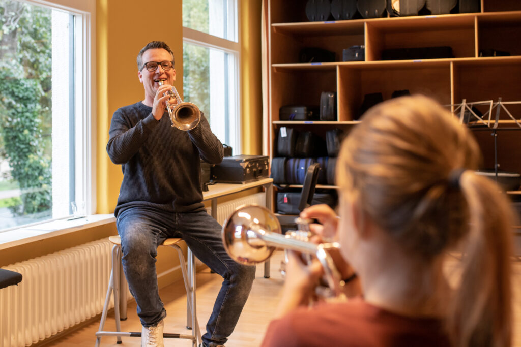 Muziekdocent geeft trompetles aan leerling en laat vrolijk zien hoe leuk werken bij Planck is.